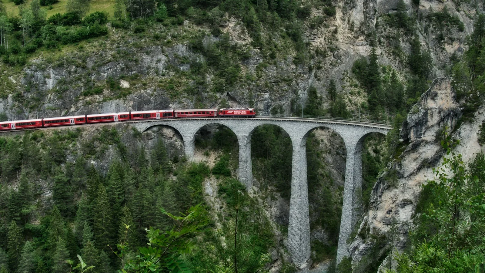Train rouge des Chemins de fer rhétiques traversant un viaduc de pierre dans les Grisons